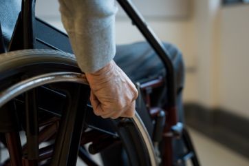 Paralyzed old man using his wheelchair. Closeup of hand of disabled man pushing wheel of wheelchair. Detail of hand of senior man holding the wheel of wheelchair.